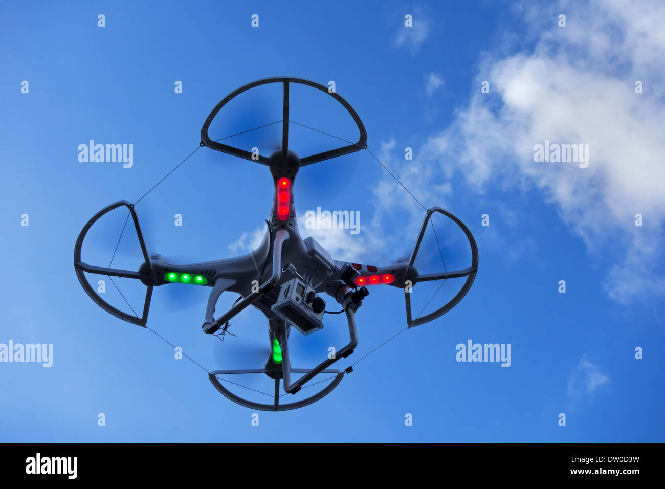 Miniature drone / unmanned aerial vehicle / UAV equipped with camera in flight against blue sky with clouds Stock Photo