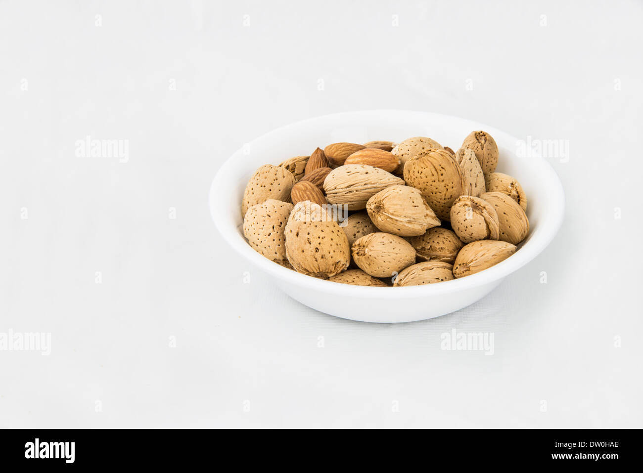 A small bowl of shelled and unshelled almonds, isolated on white. Stock Photo