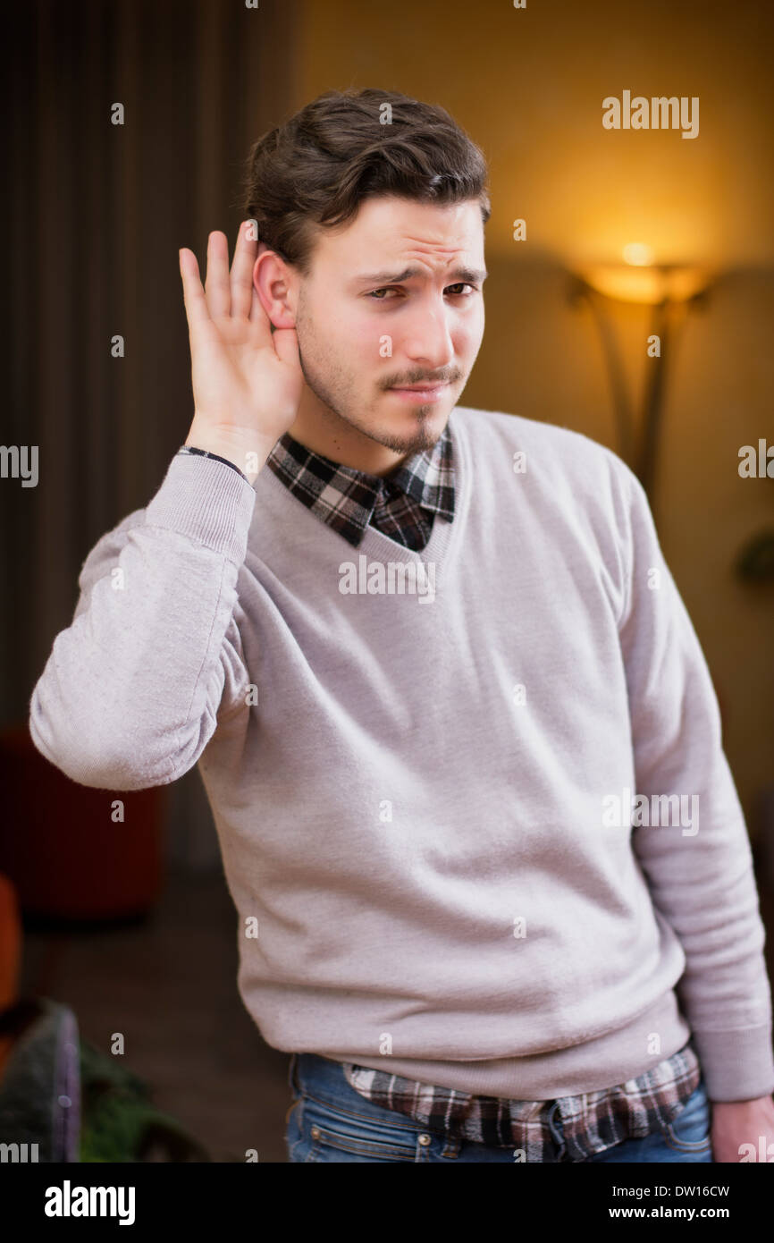 Handsome young man can't hear, putting hand around his ear. Indoors shot inside a house Stock Photo
