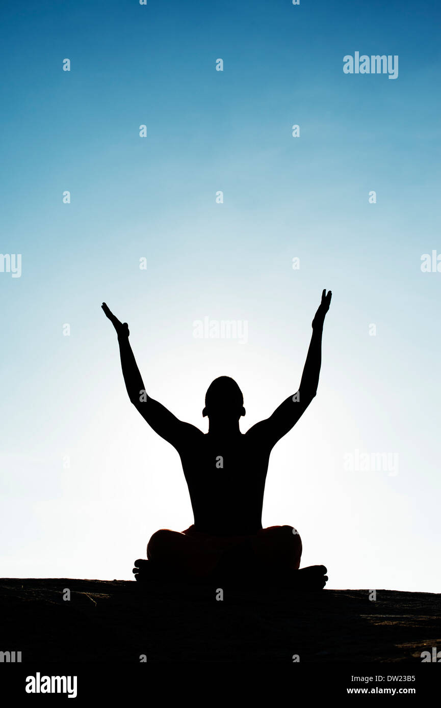 Indian man with arms in the air in front of sun and blue sky. Silhouette Stock Photo