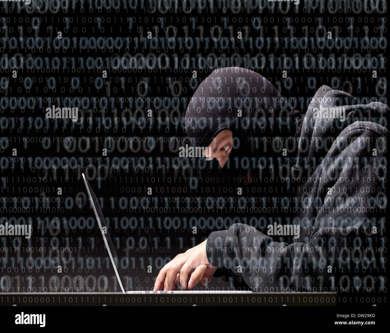 Computer hacker in a balaclava working in the darkness stealing data and personal identity information off a laptop computer Stock Photo
