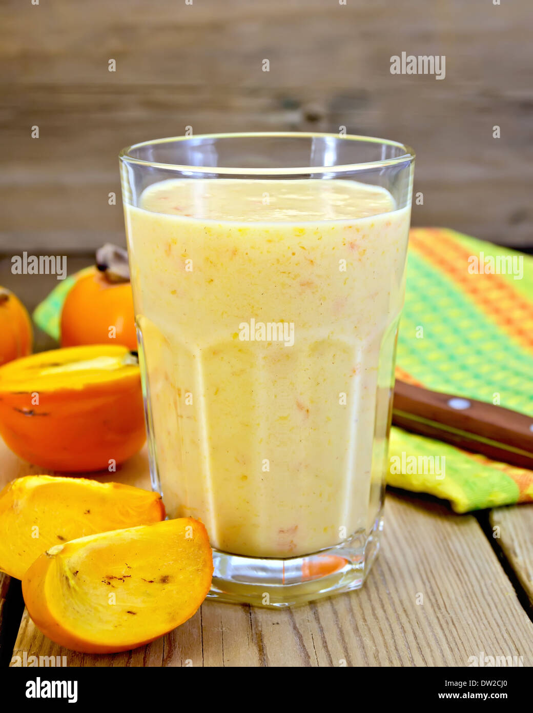 Milkshake in a glass with persimmons, napkin, knife on background wooden plank Stock Photo
