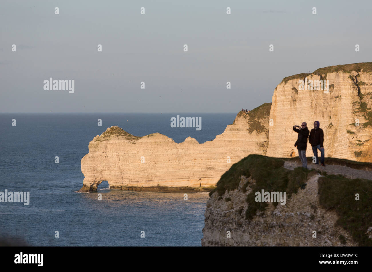 Couple taking a picture near the Porte d'Amont. Natural arche in the Étretat falaises, cliffs. Stock Photo
