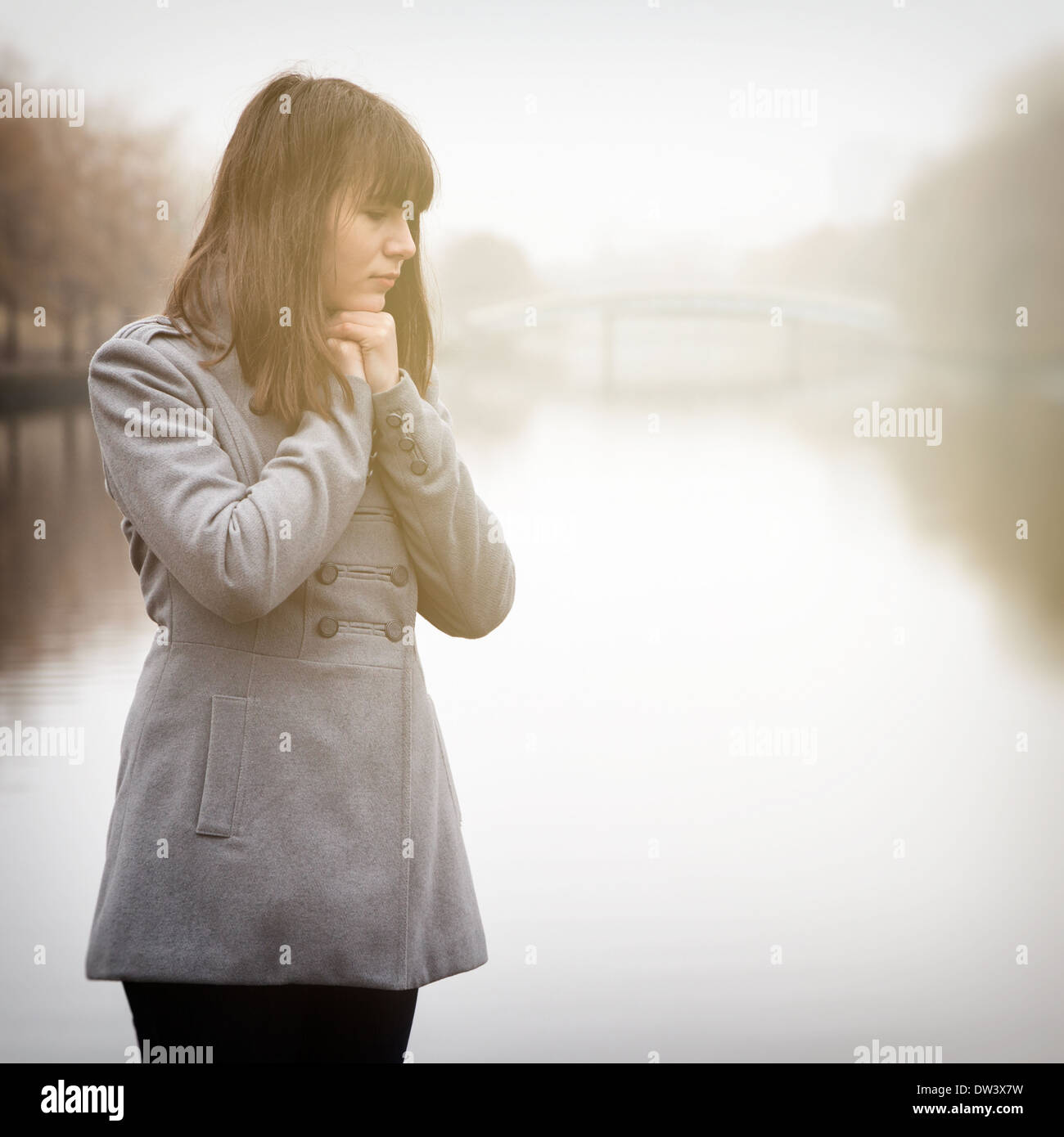 young pretty sad girl in cold weather near river in a fog Stock Photo