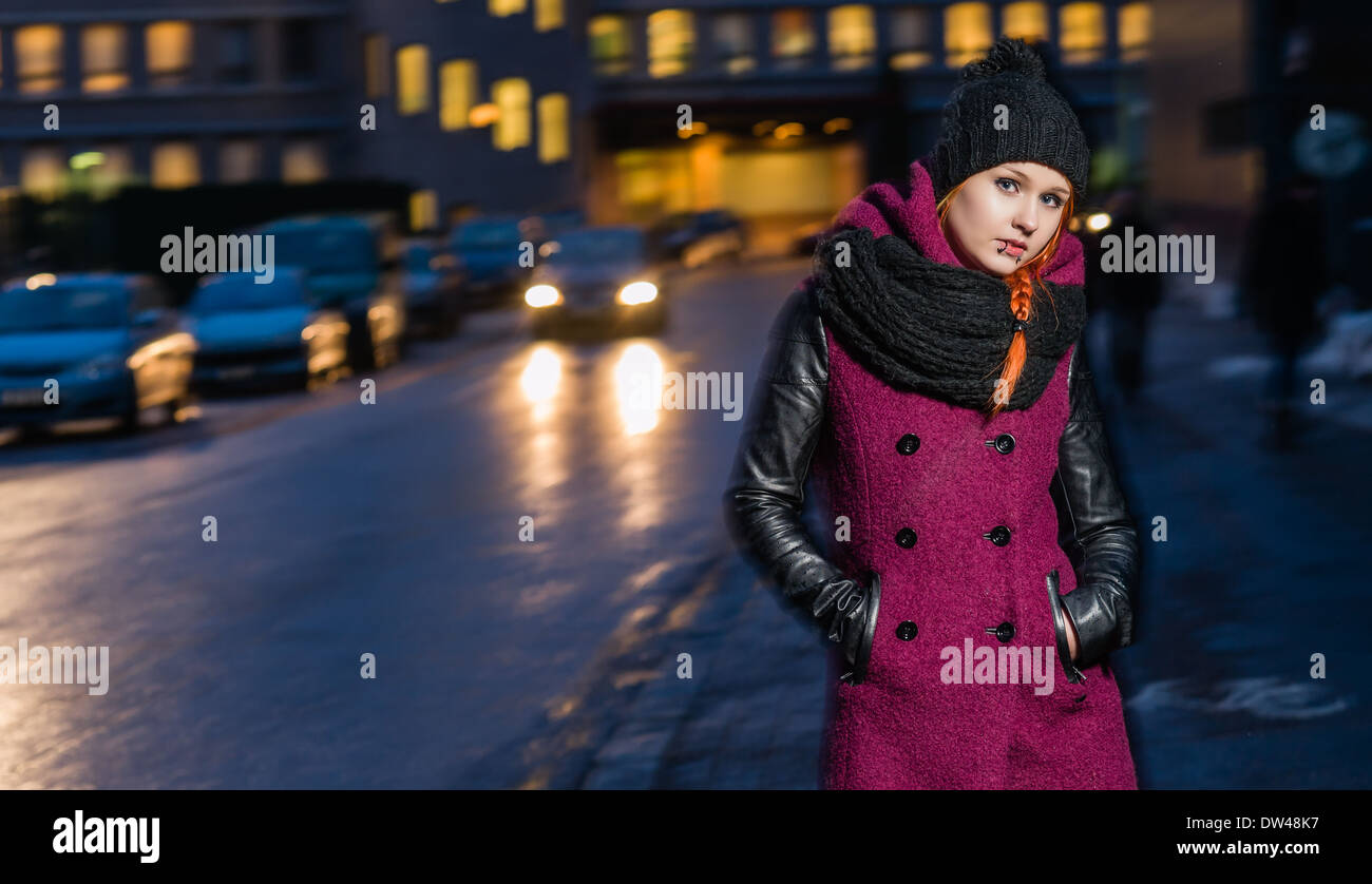 Attractive woman wearing winter coat, city evening on background, focus on foreground Stock Photo