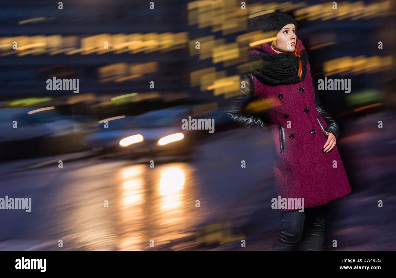 Attractive woman wearing winter coat, city evening on background, long exposure and flash Stock Photo