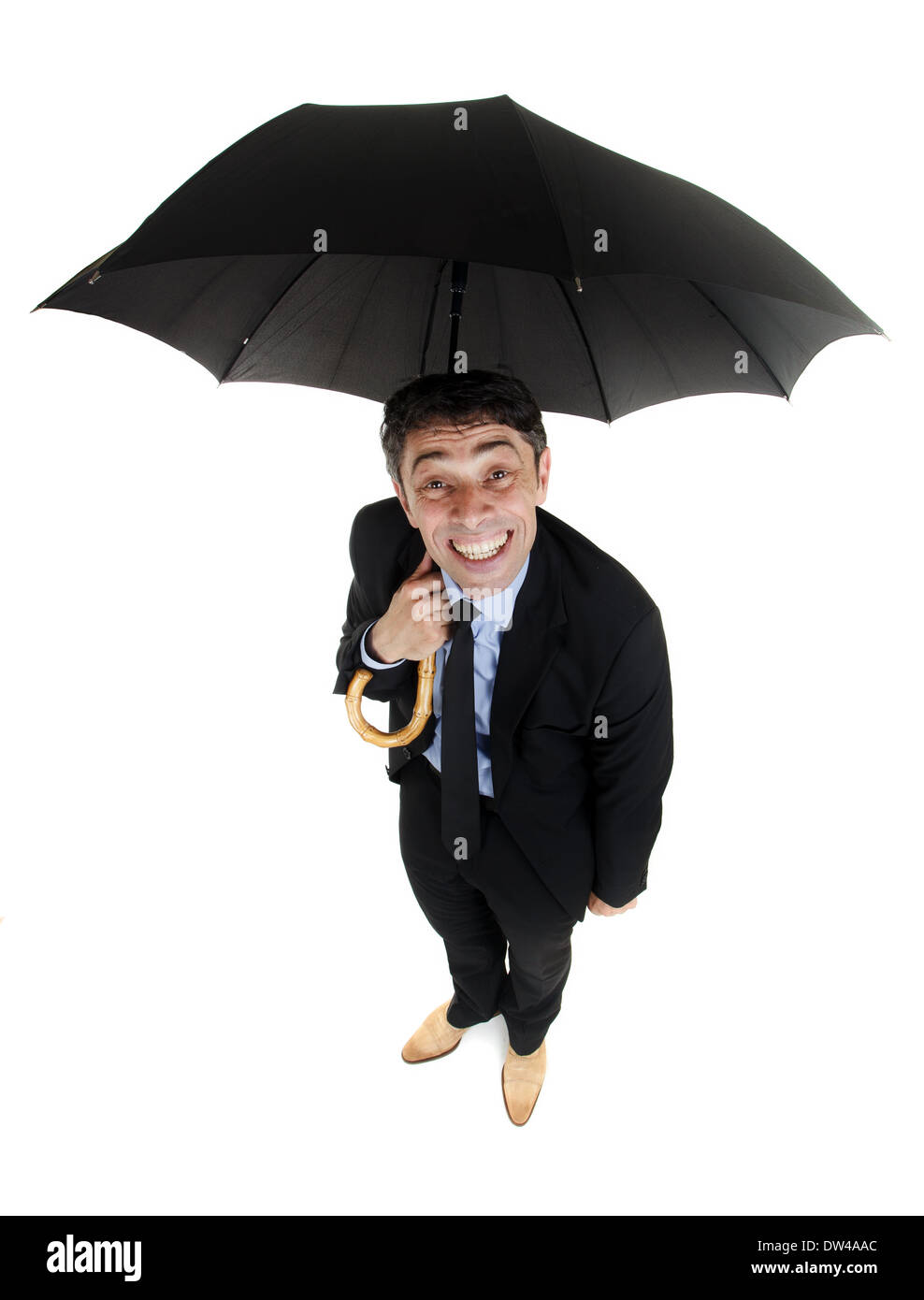Obsequious businessman sheltering under an umbrella looking up at the camera from underneath with a cheesy insincere smile, high Stock Photo
