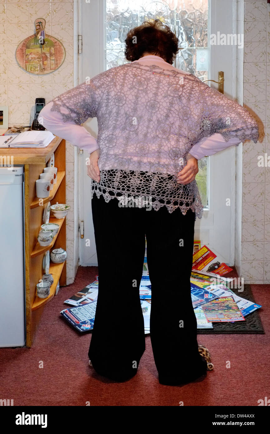 elderly woman looking at a huge pile of junk mail that has been put through the letter box in her front door Stock Photo
