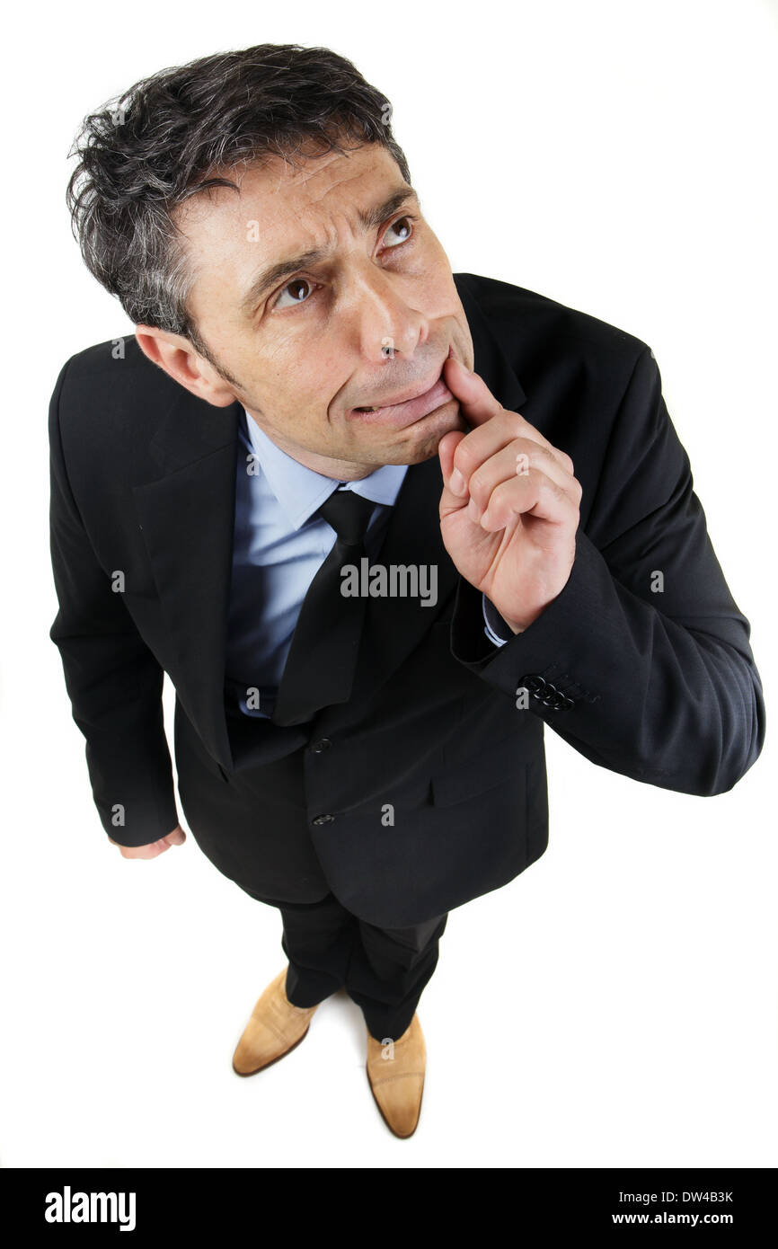 high angle full length portrait of a thoughtful frowning businessman standing looking up with his finger to his mouth Stock Photo