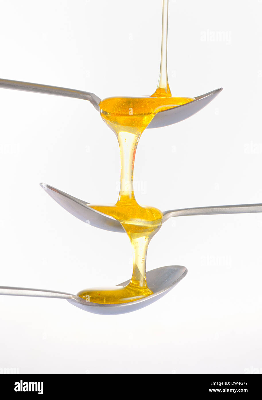 honey falling over three teaspoons on white background Stock Photo