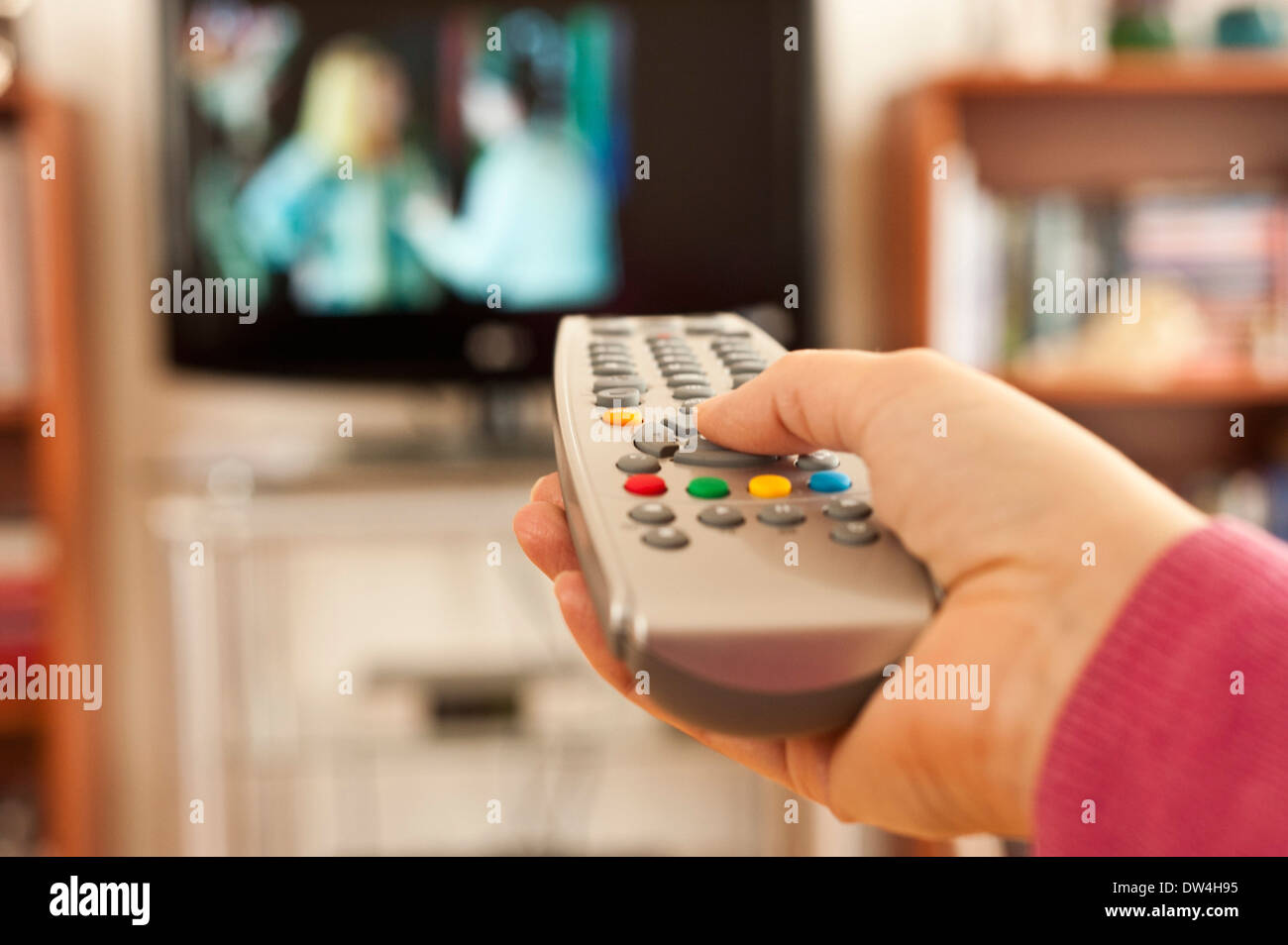 hand holding a remote control in front of television screen Stock Photo