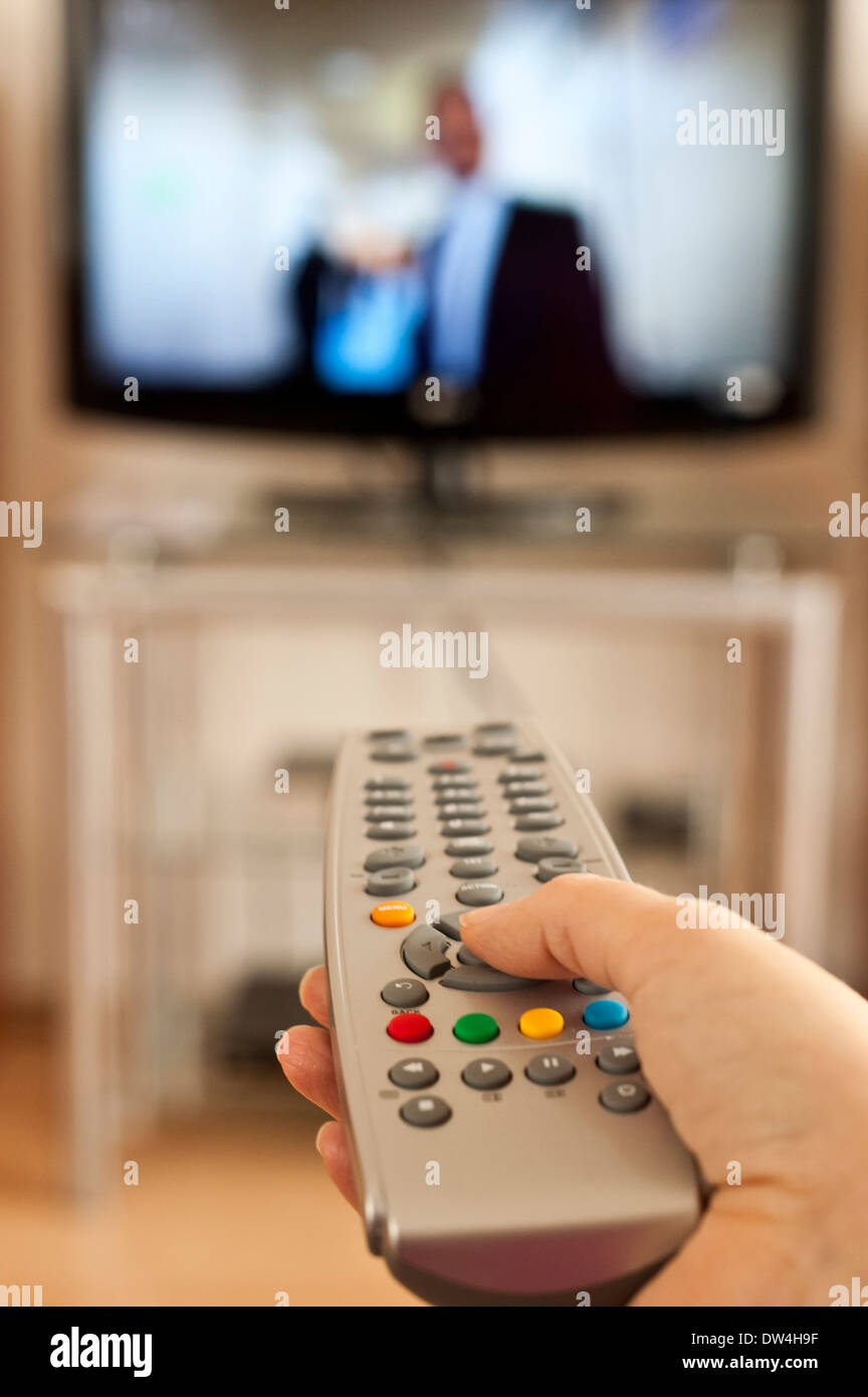 hand holding a remote control in front of television screen Stock Photo