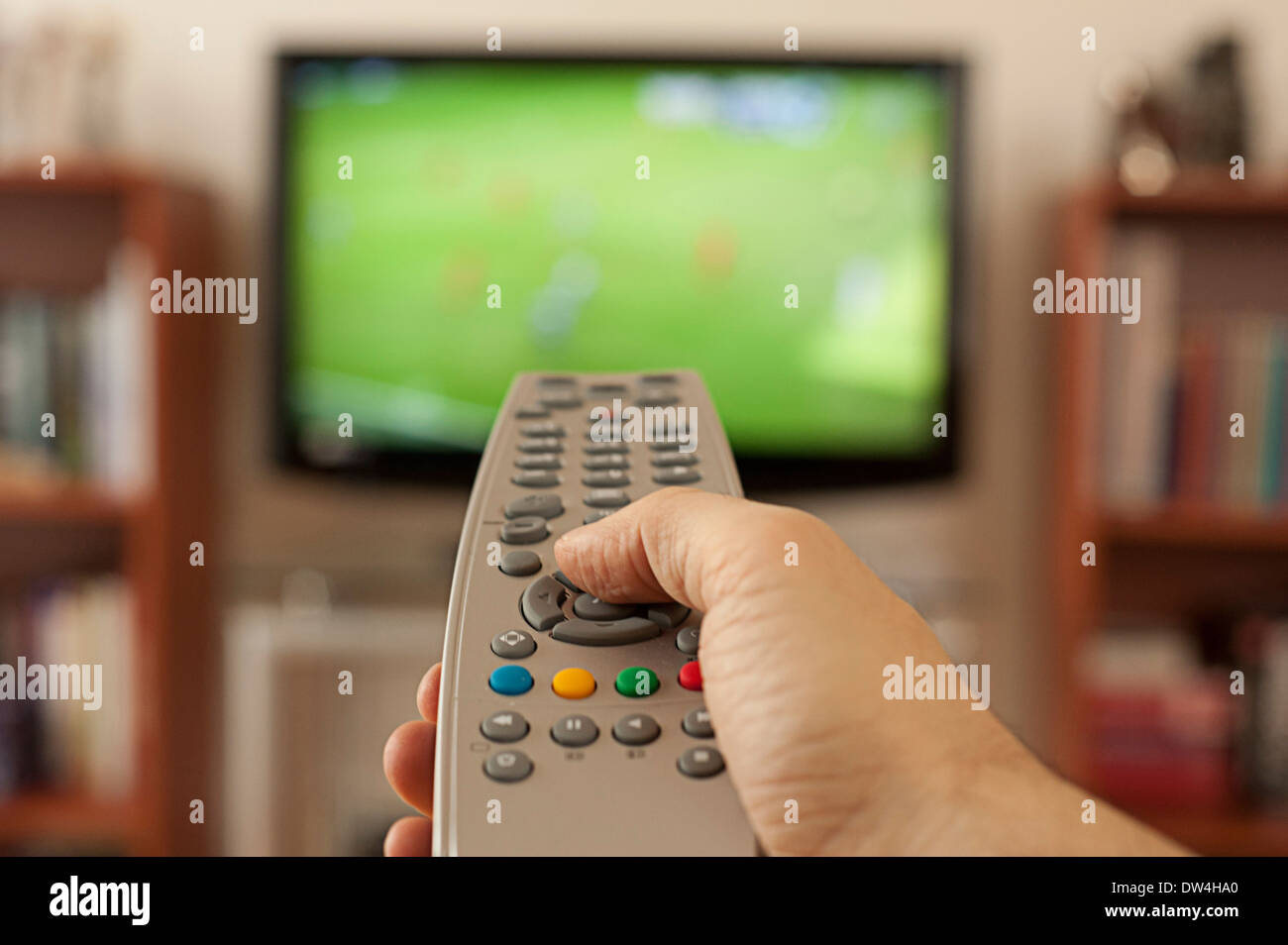 hand holding a remote control in front of television screen Stock Photo