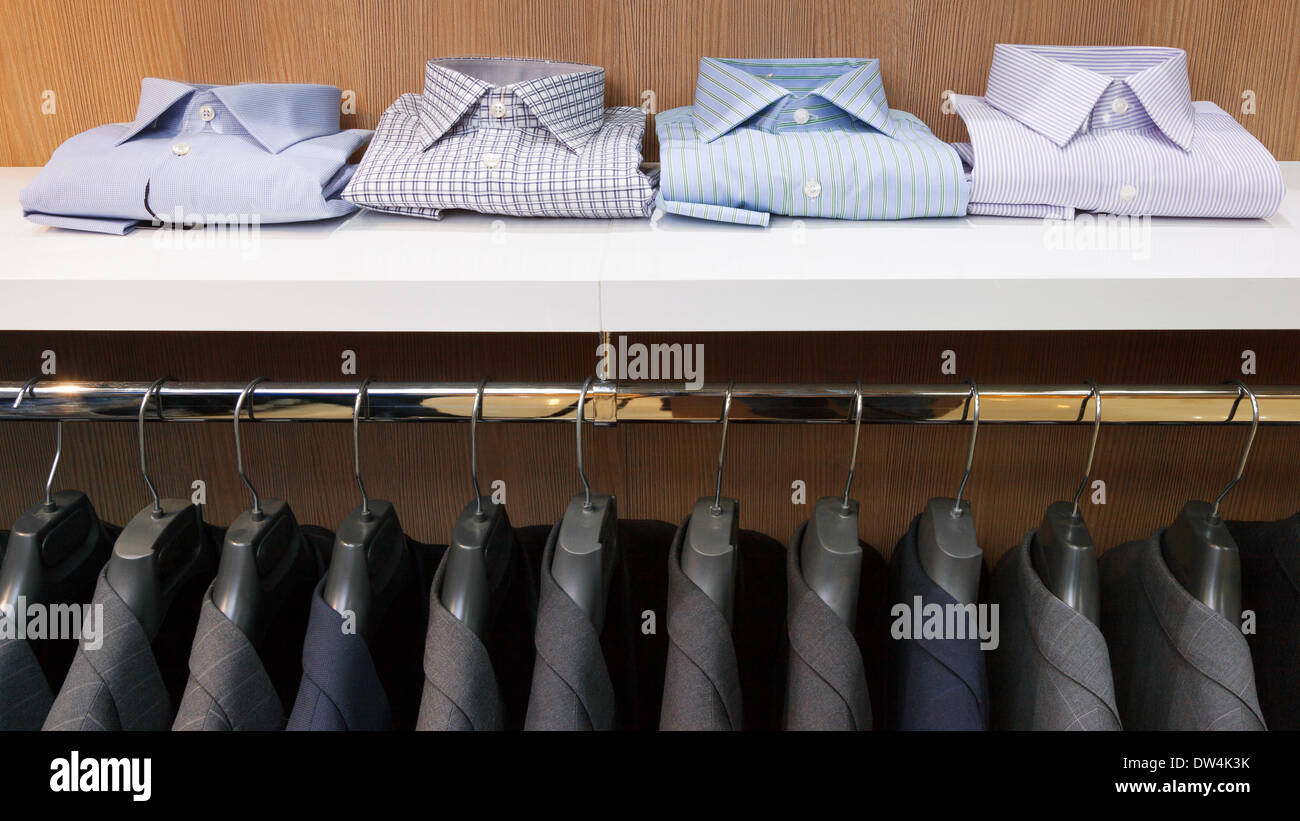 Row of men suit jackets on hangers and shelf with shirt in clothing store Stock Photo