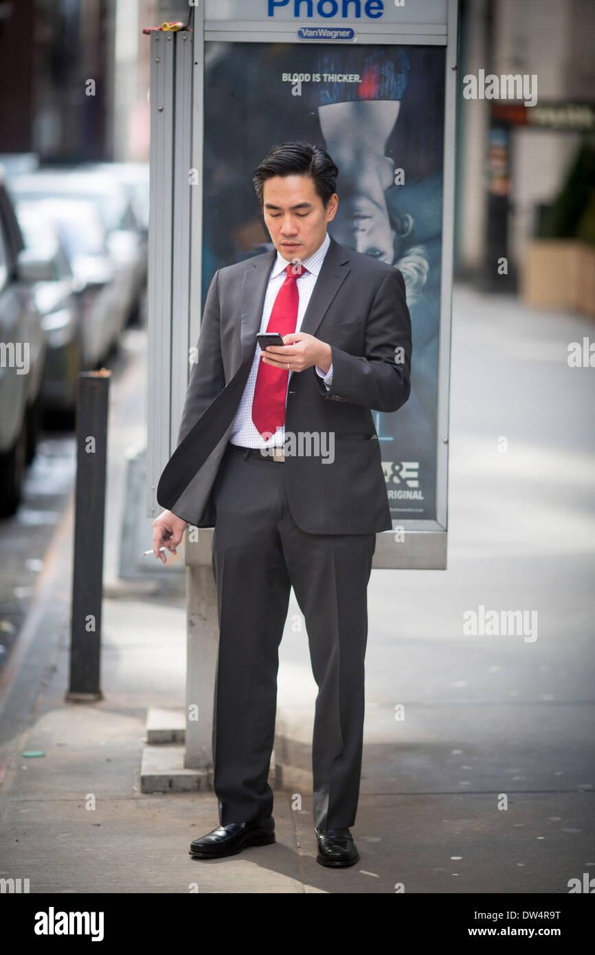 Manhattan New York city in North America, Pictured Asian man smoking in the street and texting on his mobile phone Stock Photo