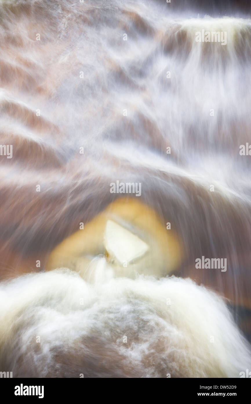 Piece of slightly yellowish ice under brownish flowing water in winter ...