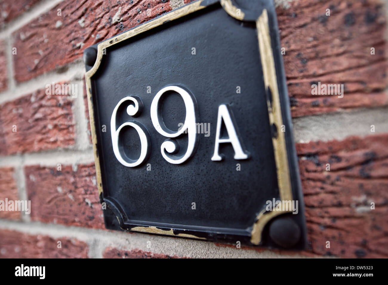 The number 69 with the suffix A on a painted brass plaque attached to a red brick wall Stock Photo