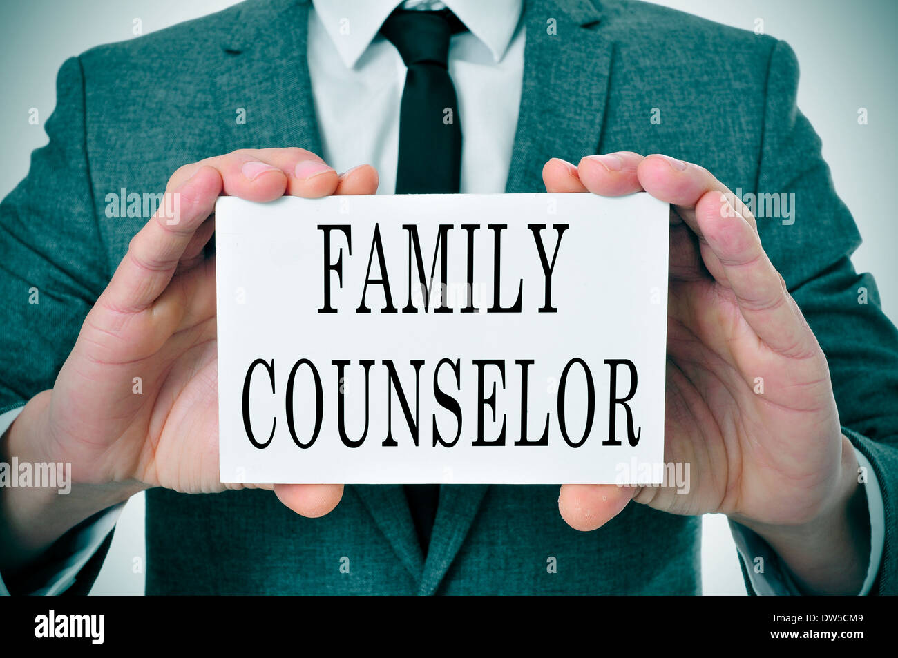 a man wearing a suit sitting in a desk with a desktop nameplate in front of him with the word family counselor Stock Photo