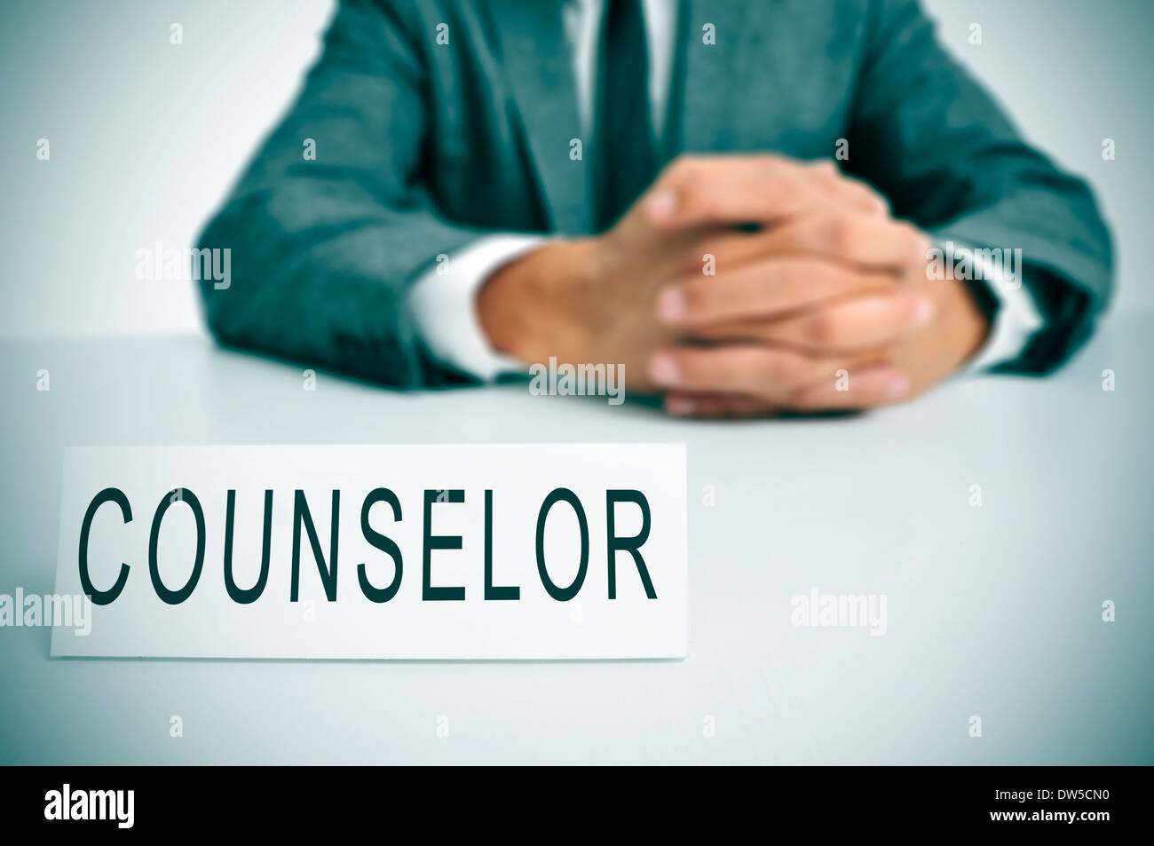 a man wearing a suit sitting in a desk with a desktop nameplate in front of him with the word counselor Stock Photo