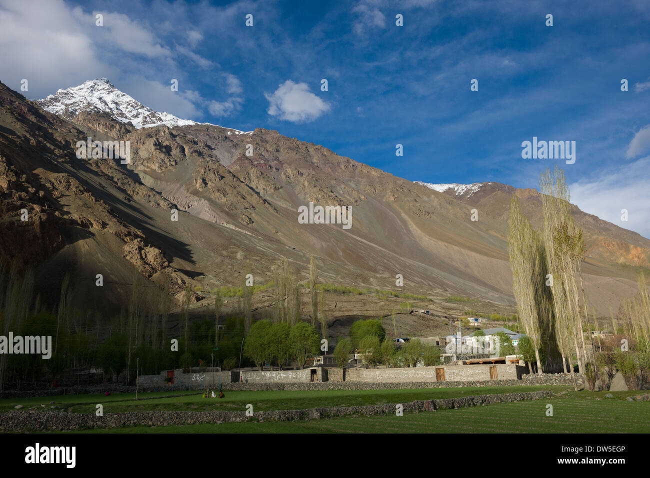 Locals sitting outside in fields outside of a walled compound, in the Ghizar River (Gilgit River) Valley near Golaghmuli, seen from the Shandur-Gilgit Road, near the Shandur Pass, Gilgit-Baltistan, Pakistan Stock Photo