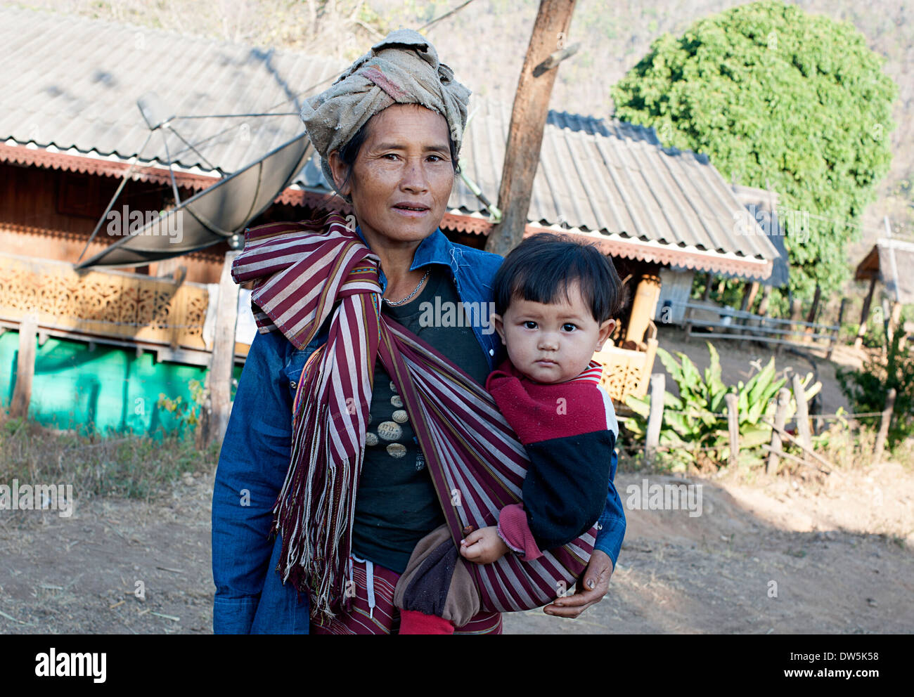 Karen Hill Tribe woman carrying son in sling stops for photo in Blay Doh Key village, northern Thailand. Stock Photo