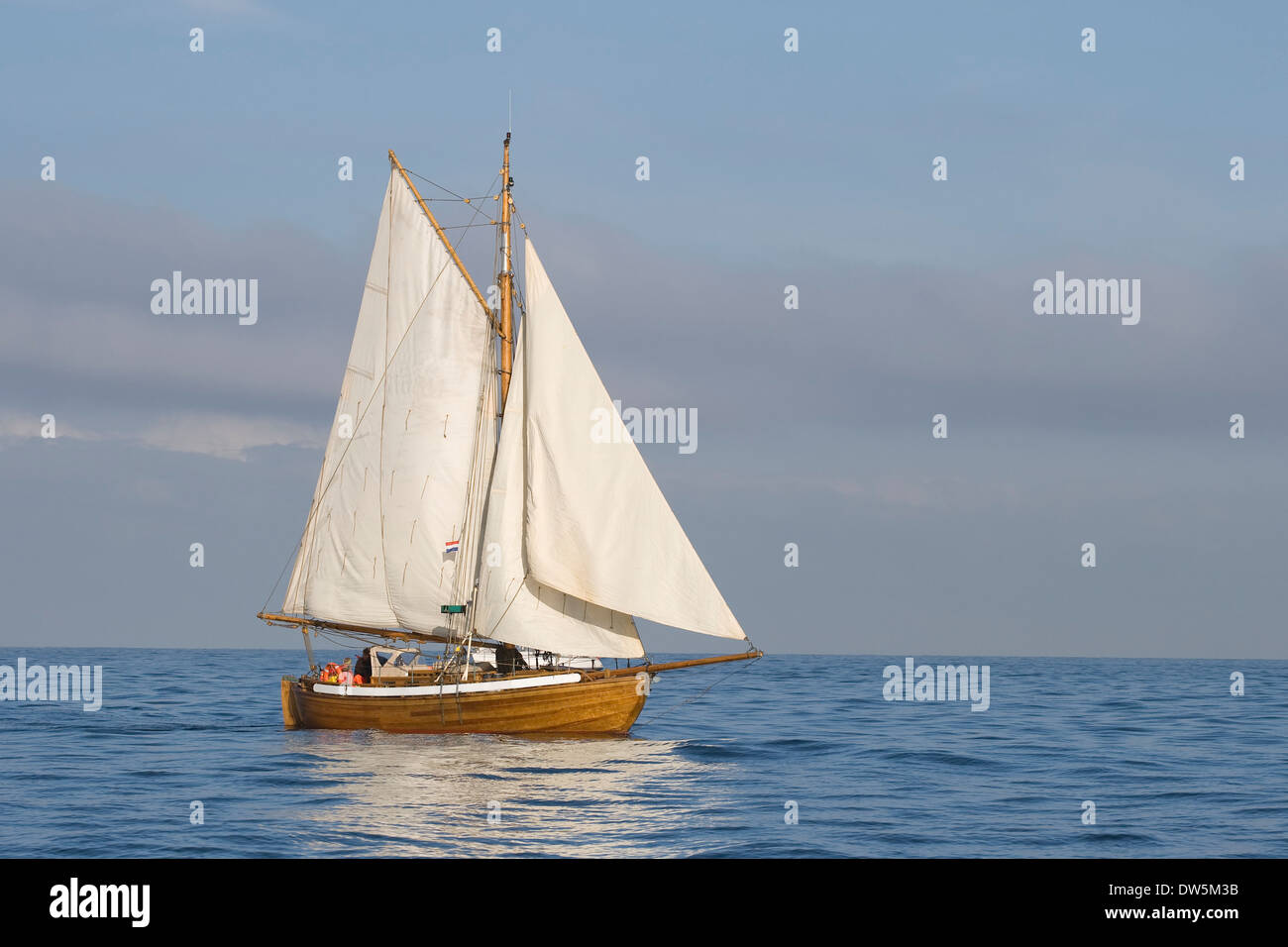 Tender with white sails in the calm sea Stock Photo