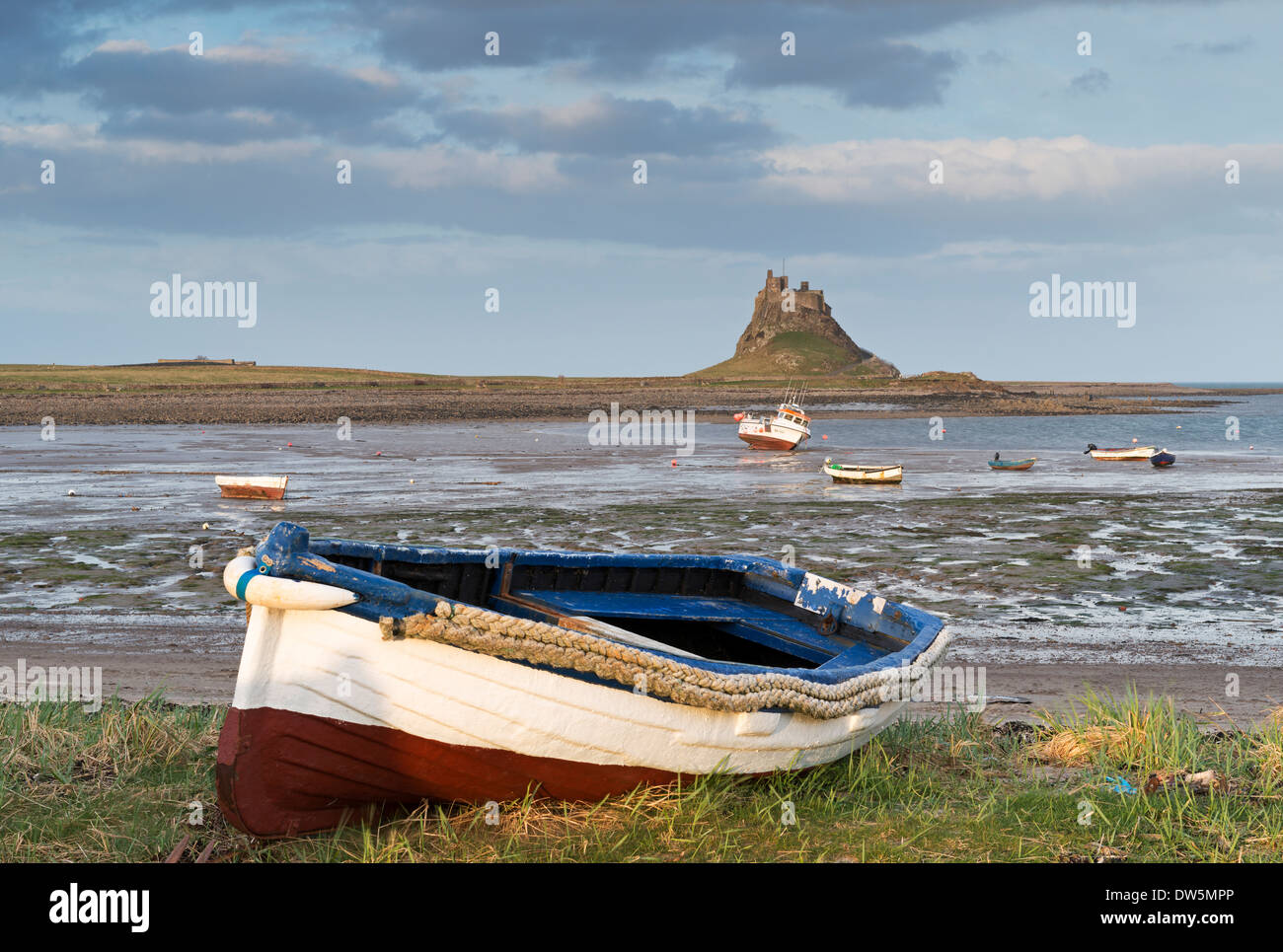 Fishing boat pulled onto the shore at Holy Island, looking towards the castle, Lindisfarne, Northumberland, England. Stock Photo