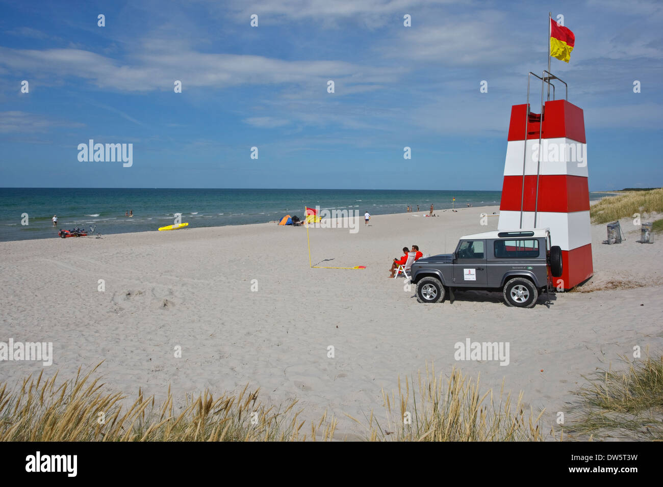 The sandy beach with lifeguards at the coast of Kattegat by Roervig flag that marks the zone of lifeguard and tower Stock Photo