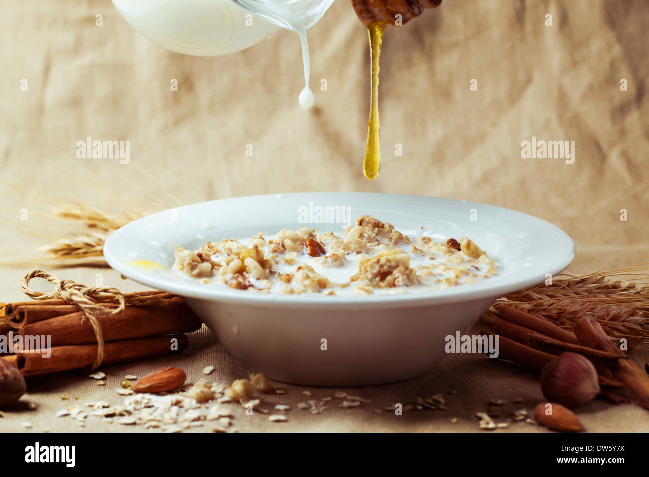 Plate of muesli with pouring milk and honey, cinnamon and nuts over