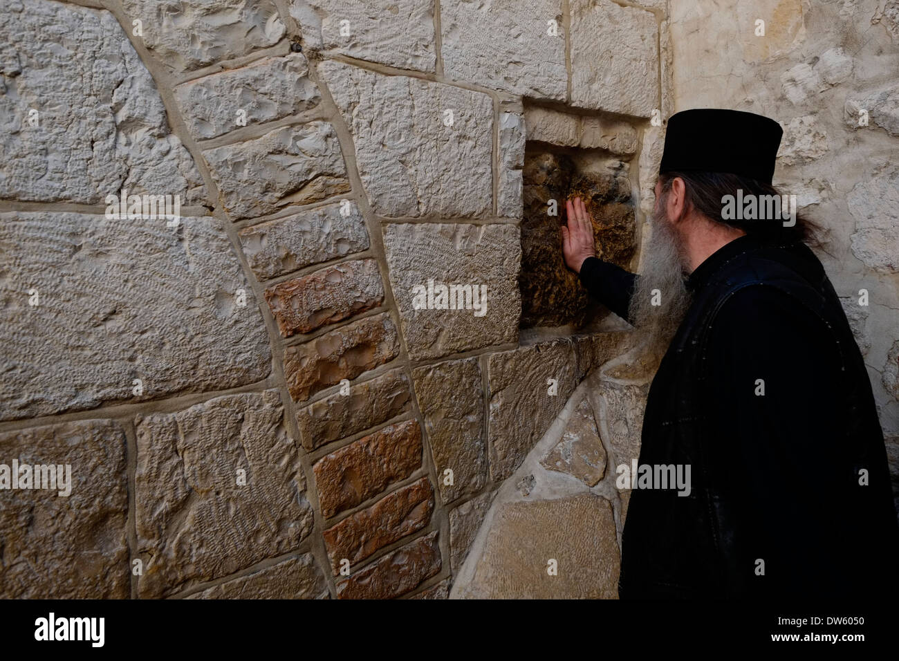 An Eastern Orthodox priest puts his palm on a square stone believed to be imprint of Jesus hand on the sunken part of the exterior wall of the Chapel of Simon of Cyrene, at the 5th station of the cross in Via Dolorosa street old city East Jerusalem Israel Stock Photo