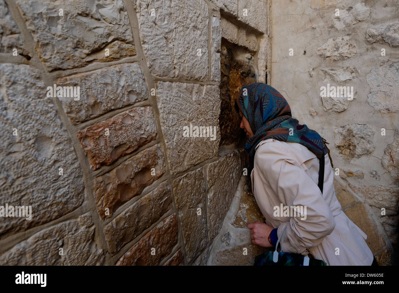 An Eastern Orthodox Christian prays as she puts her palm on a square stone believed to be imprint of Jesus hand on the sunken part of the exterior wall of the Chapel of Simon of Cyrene, at the 5th station of the cross in Via Dolorosa street old city East Jerusalem Israel Stock Photo