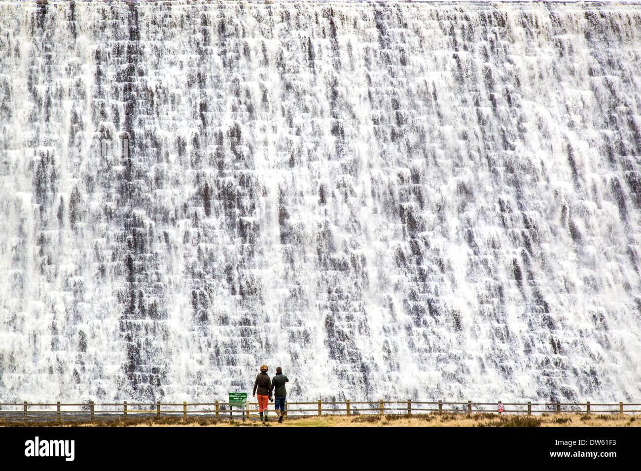 A couple watch water overflowing over the Derwent Reservoir dam wall in the Derbyshire Peak District after weeks of heavy rain Stock Photo