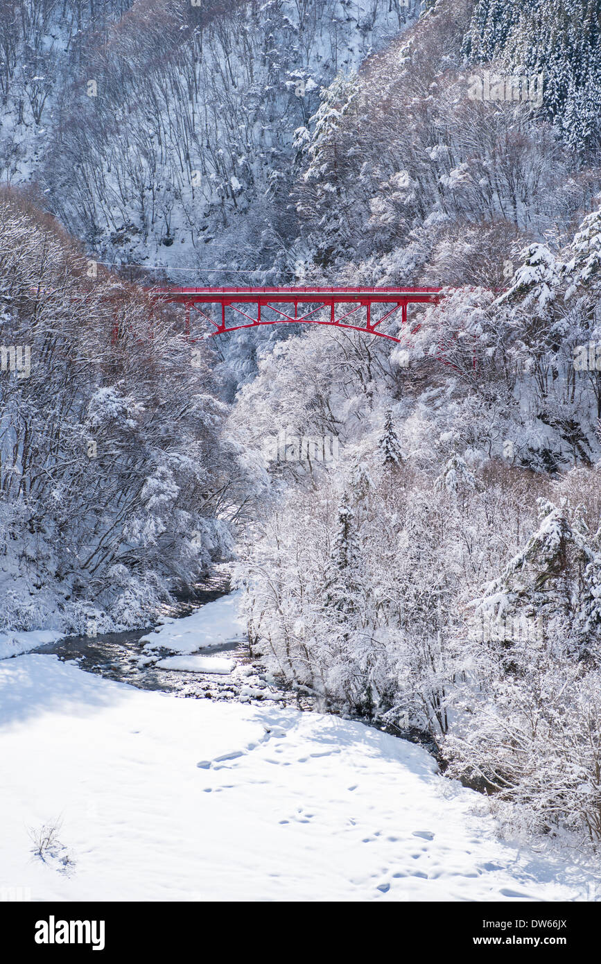 A red bridge spanning a snow covered valley and tress near Yamada Onsen in Nagano, Japan Stock Photo