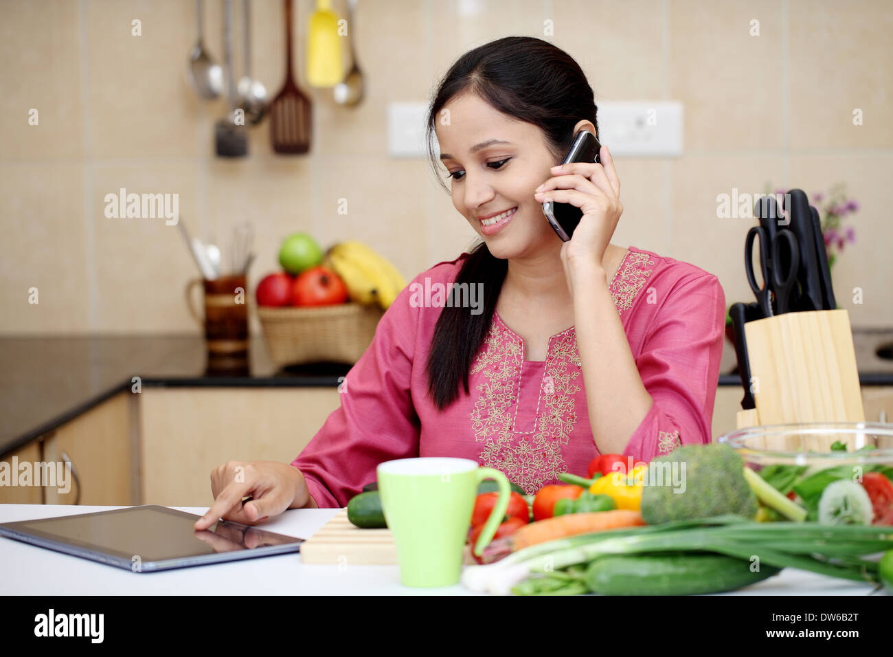 Young Indian woman working with tablet and talking on cellphone Stock Photo
