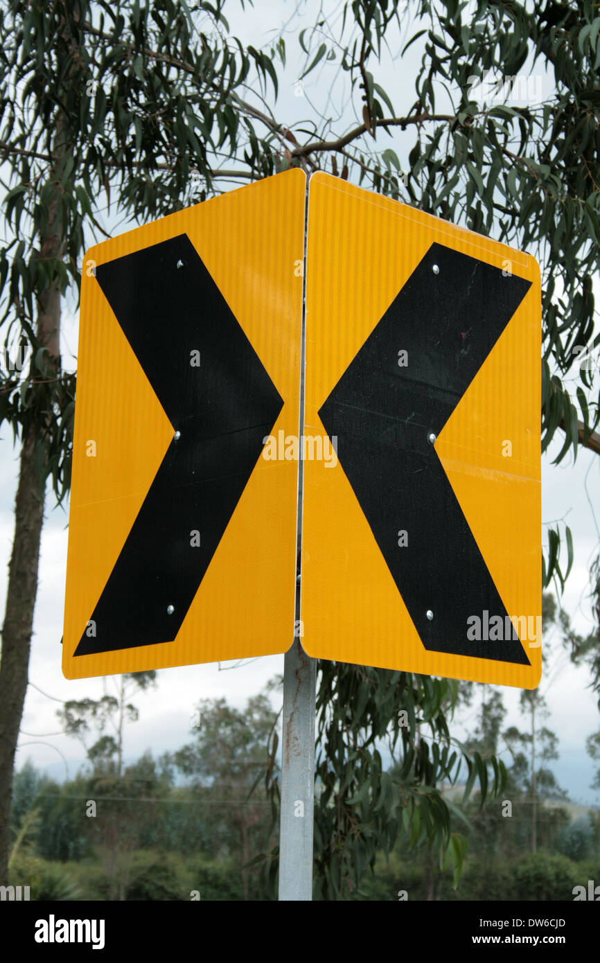 A highway sign with two converging arrows on the side of a road in
