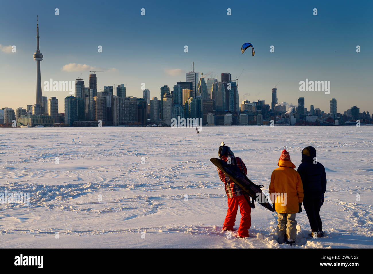 Young friends watching snowkiter with board on frozen Lake Ontario with Toronto city skyline at Toronto Islands in winter Stock Photo