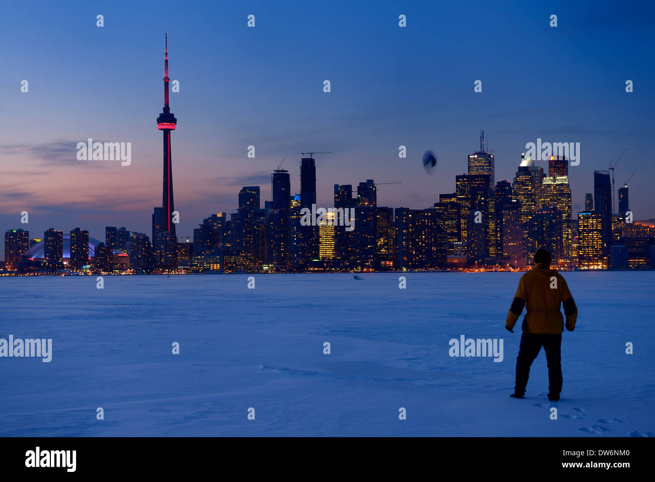 Man watching snowkite skier on frozen Lake Ontario at dusk with Toronto city skyline in winter Stock Photo