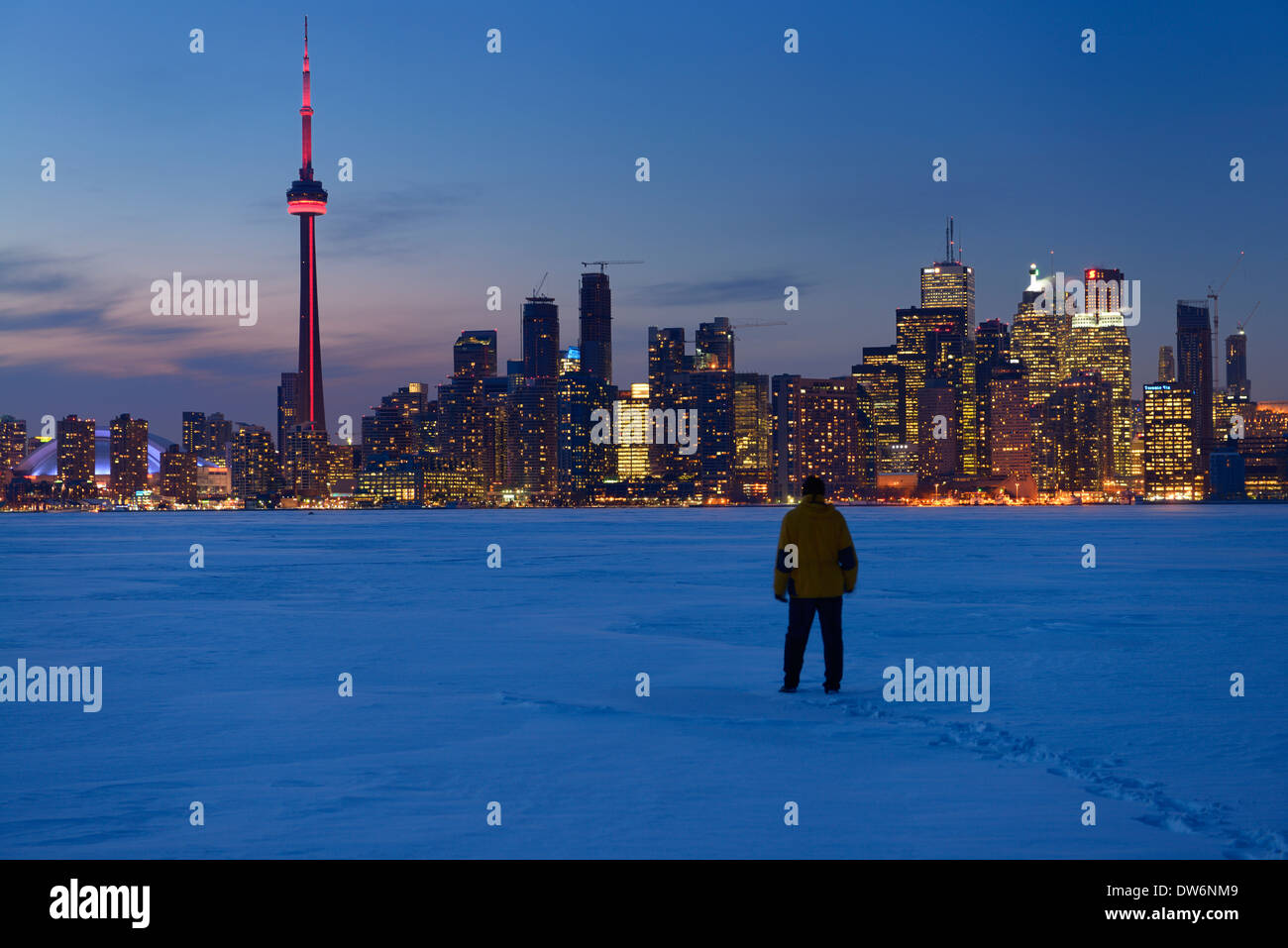 Man walking in fresh snow at dusk on frozen Lake Ontario with lights of Toronto city skyline in winter Stock Photo