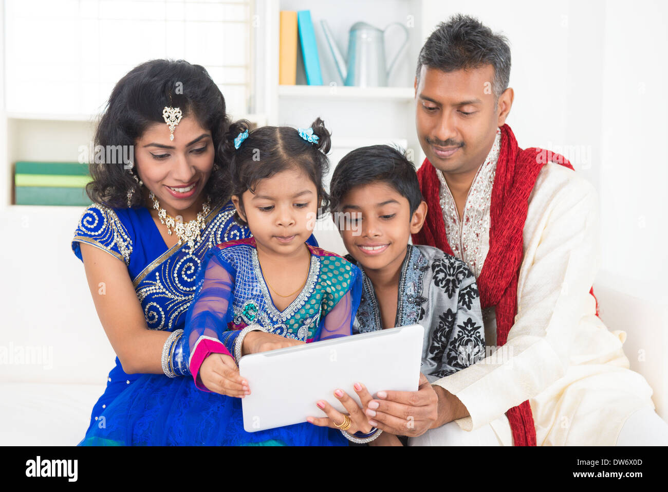 Indian Asian family using tablet pc computer at home. India family living lifestyle in traditional dress. Happy smiling parents and children. Stock Photo