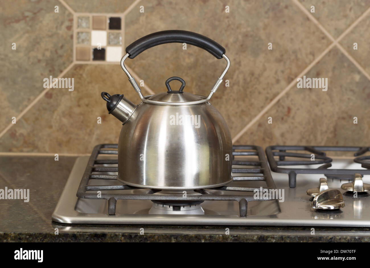 Horizontal photo of a stainless steel tea pot on stove top with stone counter tops and tile back splash Stock Photo
