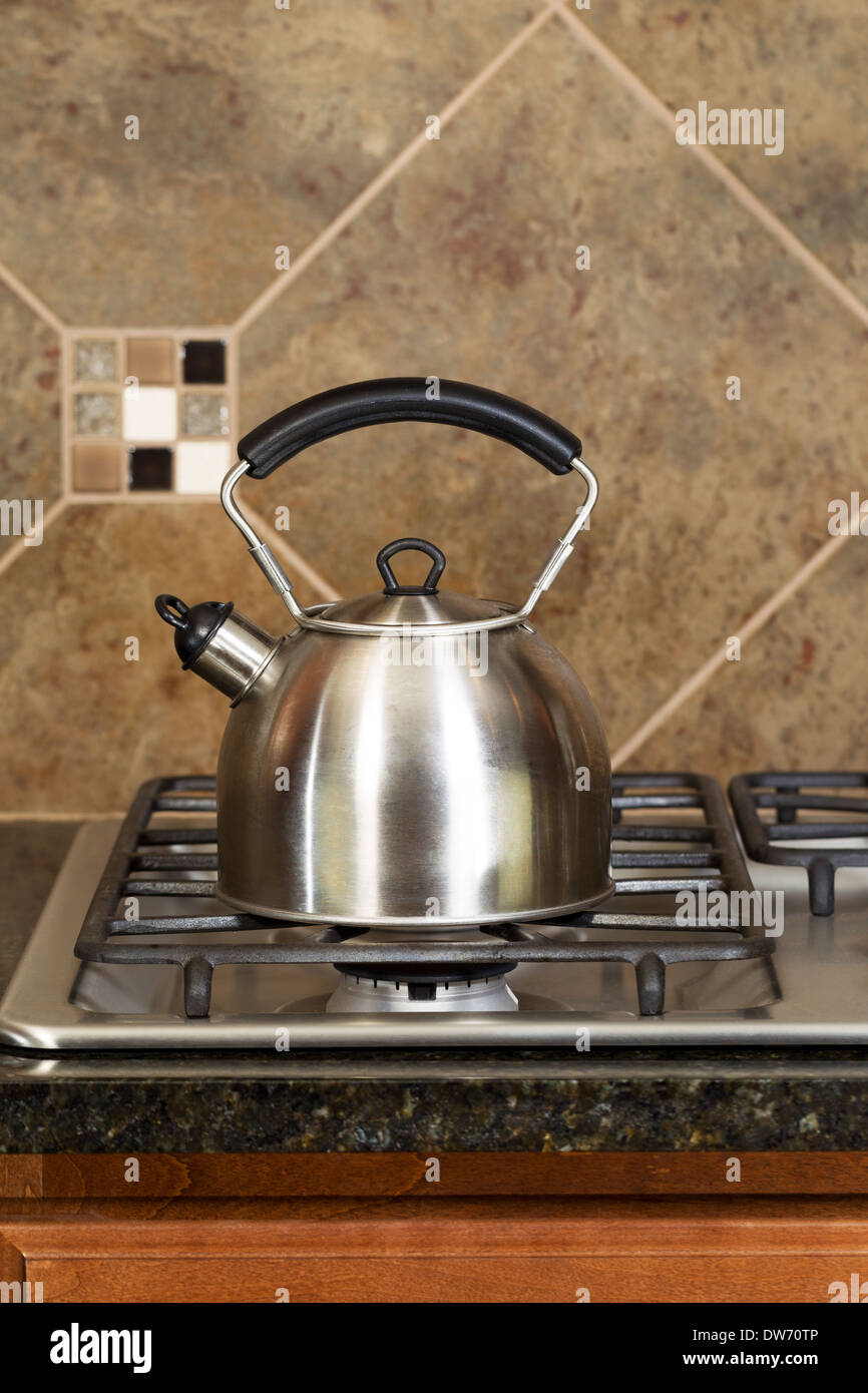 Vertical photo of a stainless steel tea pot on stove top with stone counter tops and tile back splash Stock Photo