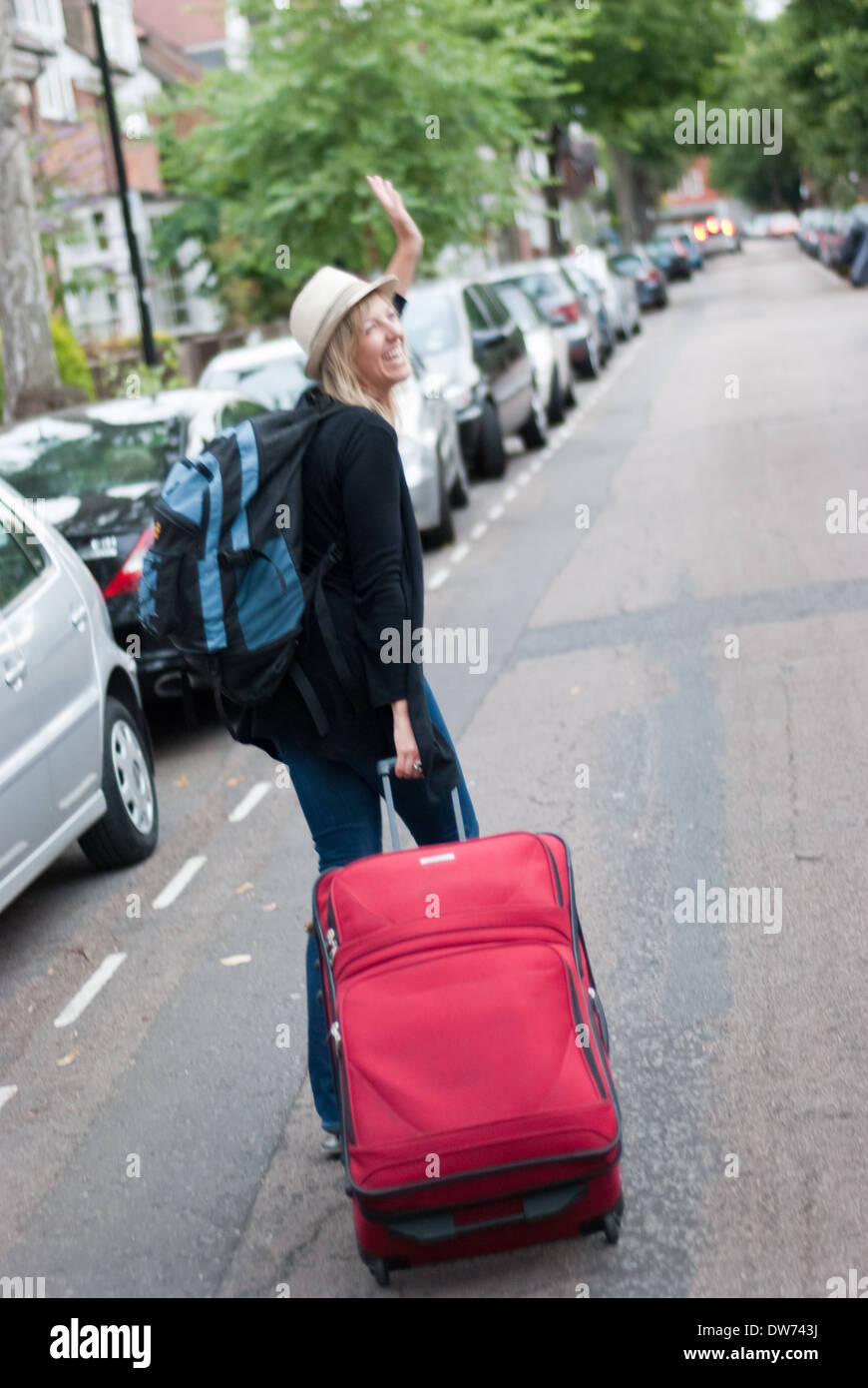 A traveler wheels her suitcase down a street in Chiswick in west London in the UK. Stock Photo