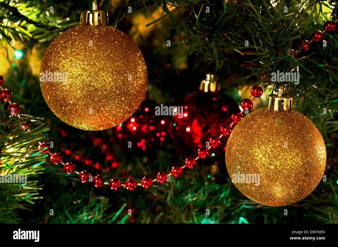 Two glittering gold ball Christmas ornaments on the tree.  With red trim and red balls, festive holiday decorations. Stock Photo
