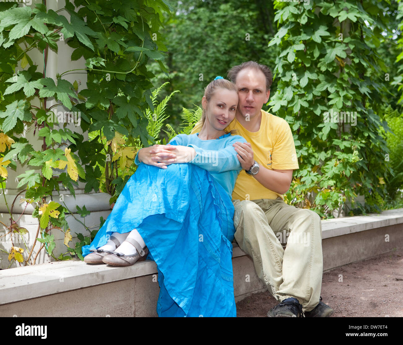 Young happy couple sits in the arbour twined greens Stock Photo