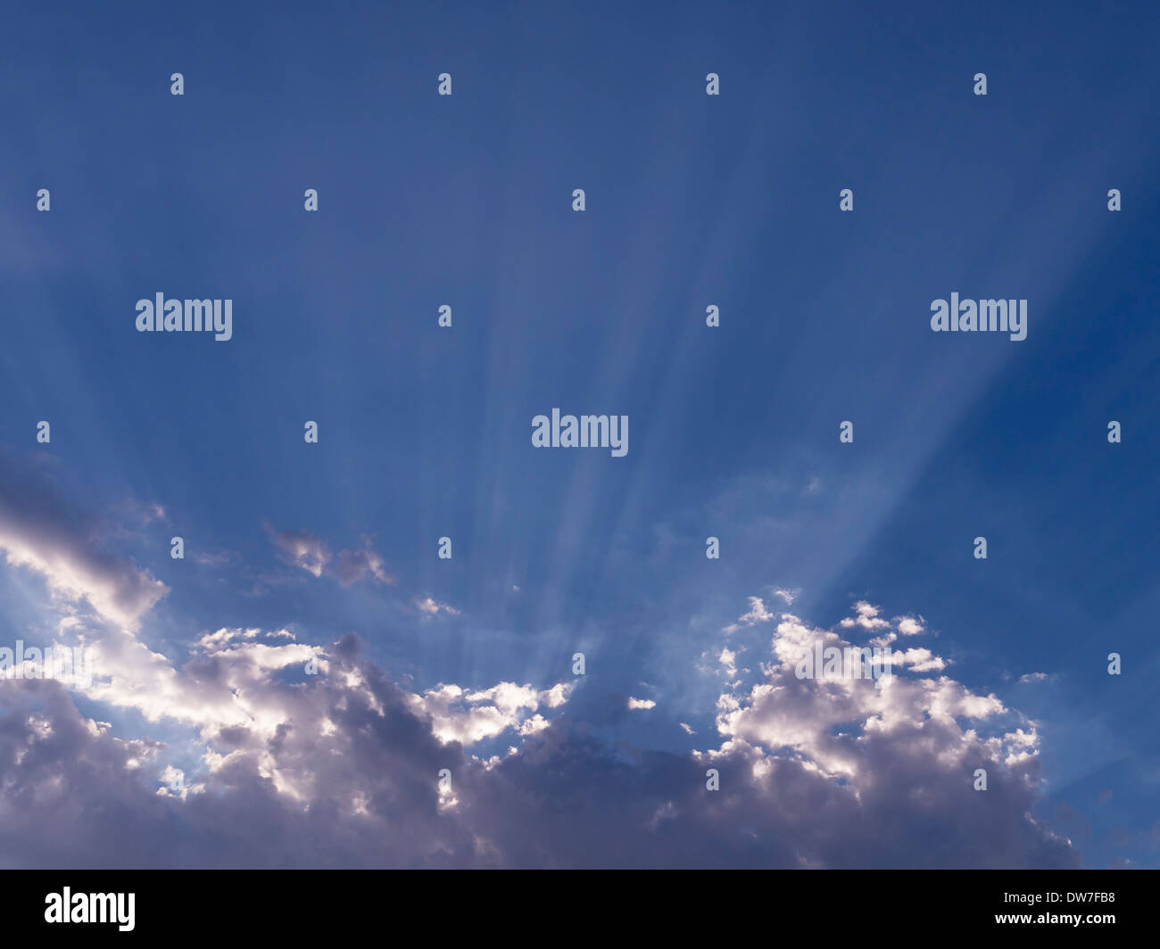 Radiating sunbeams and white clouds against blue sky Stock Photo