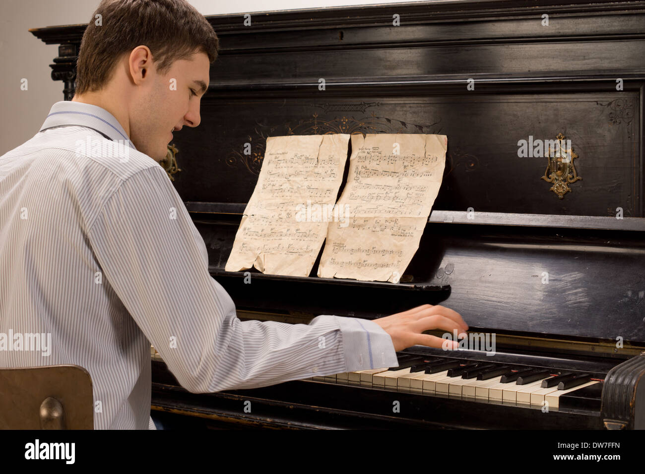 Young man having fun playing the piano smiling as he plays a melody from an  old music score on a wooden upright piano Stock Photo - Alamy