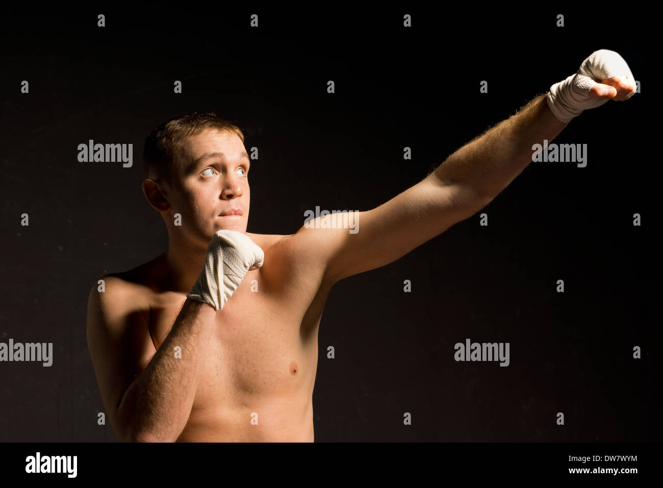 Young male boxer standing in the darkness throwing an upwards punch as
