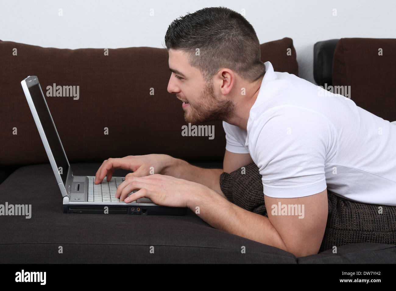 A young man is lying on a sofa and using his laptop computer Stock Photo