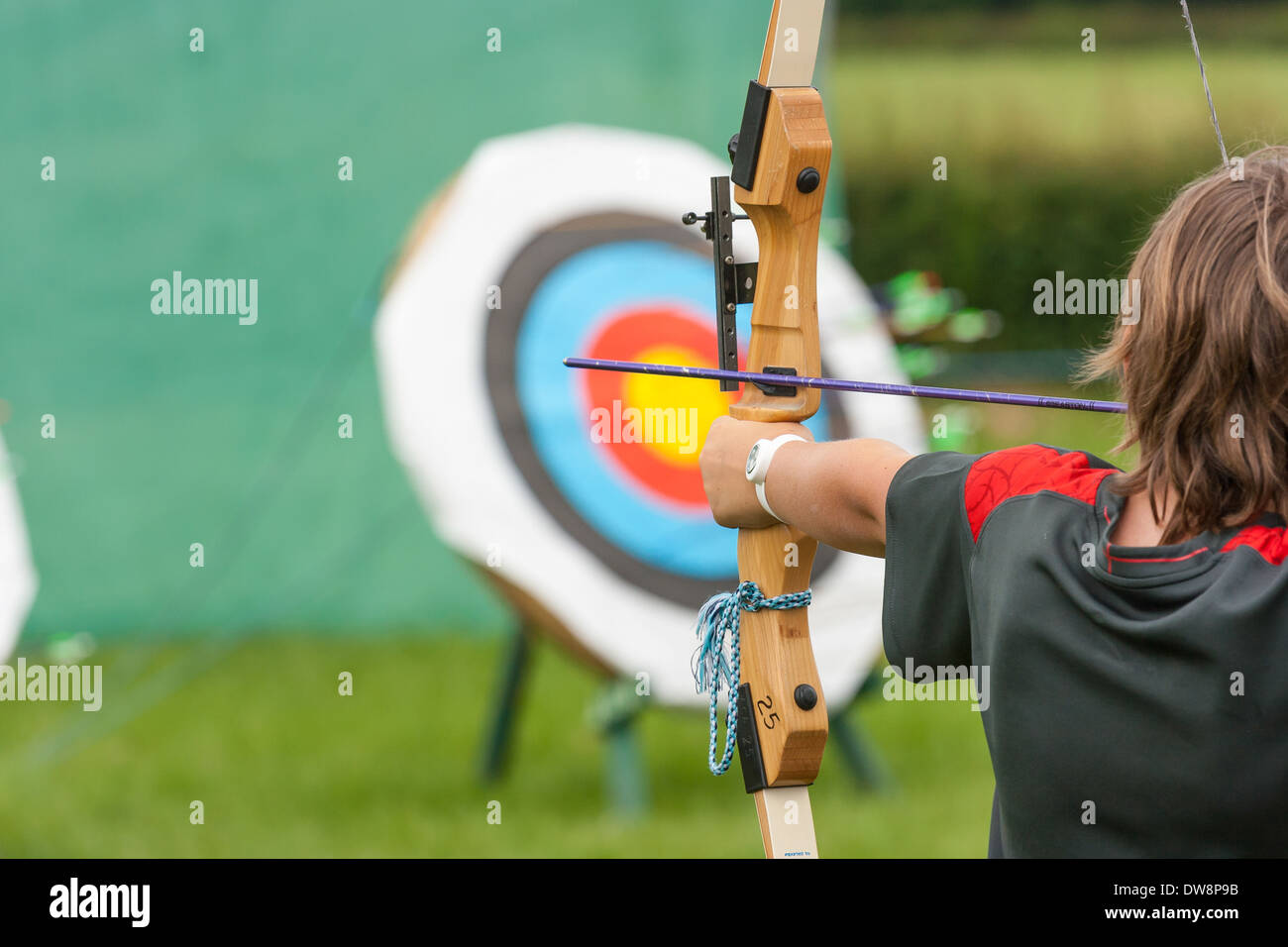 Young unknown Boy with long bow and arrow taking aim and about to shoot at target Stock Photo