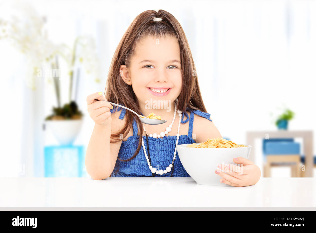 Cute little girl eating cereal from a bowl seated on table at home